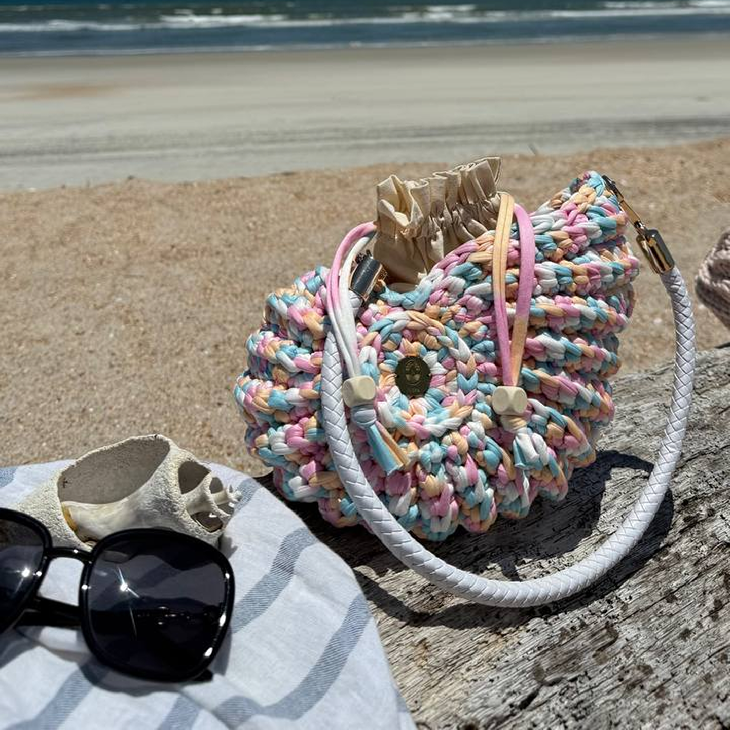 Colorful knitted bag on a beach with sunglasses and a towel