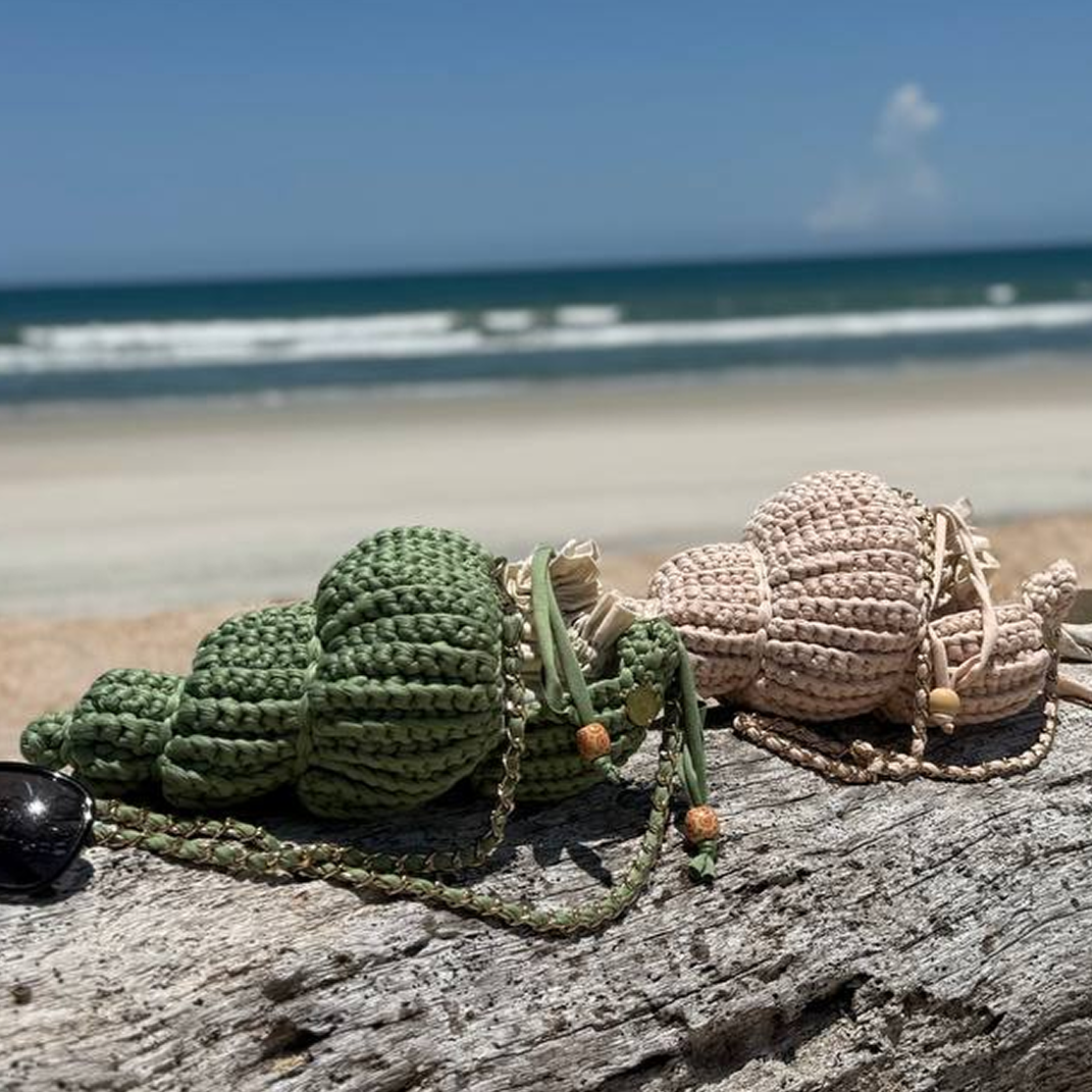 Crocheted sea turtle and shell on a log with ocean in the background